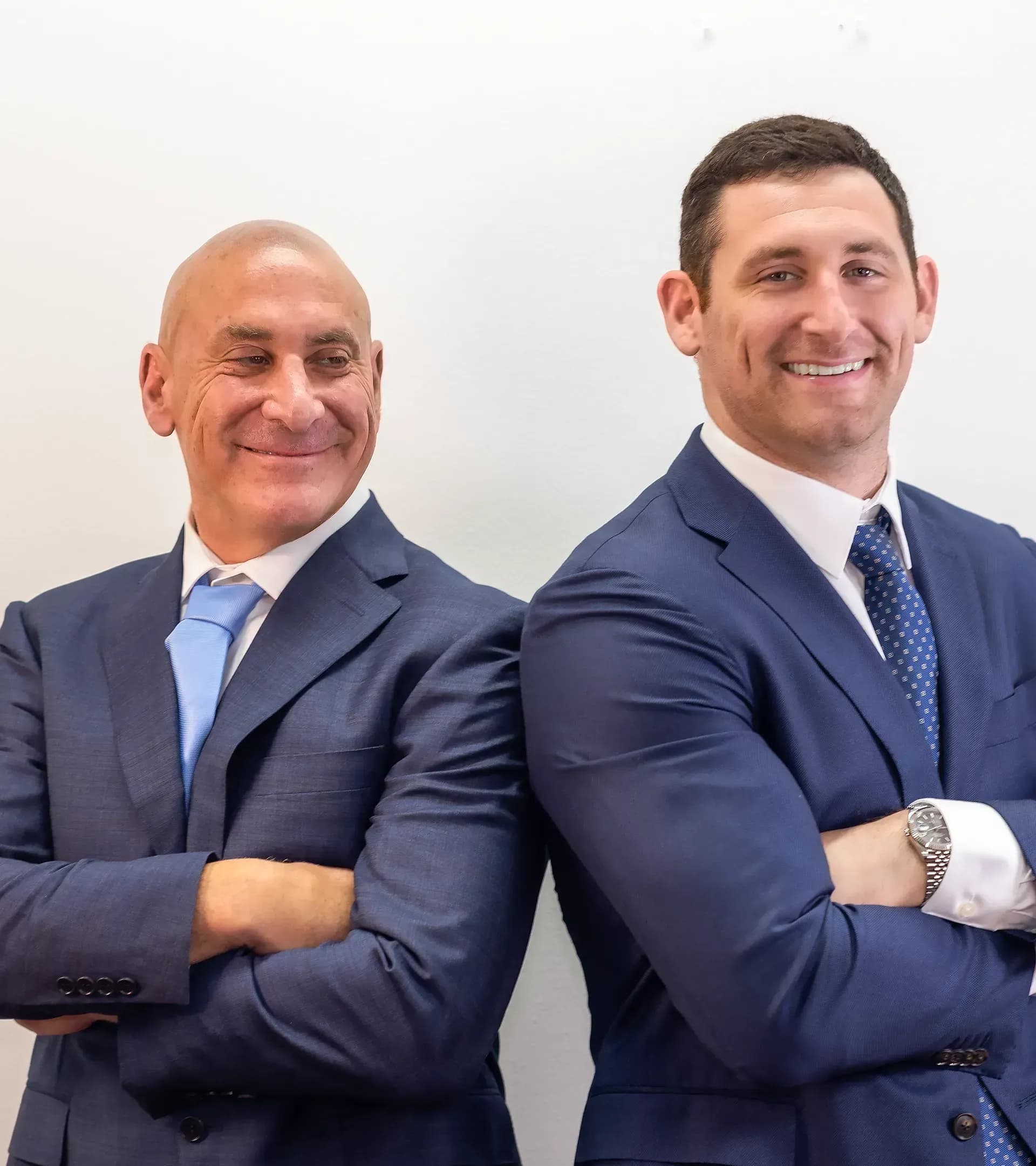Florida auto collision attorneys Scott and Alex Senf back-to-back, smiling confidently with crossed arms.