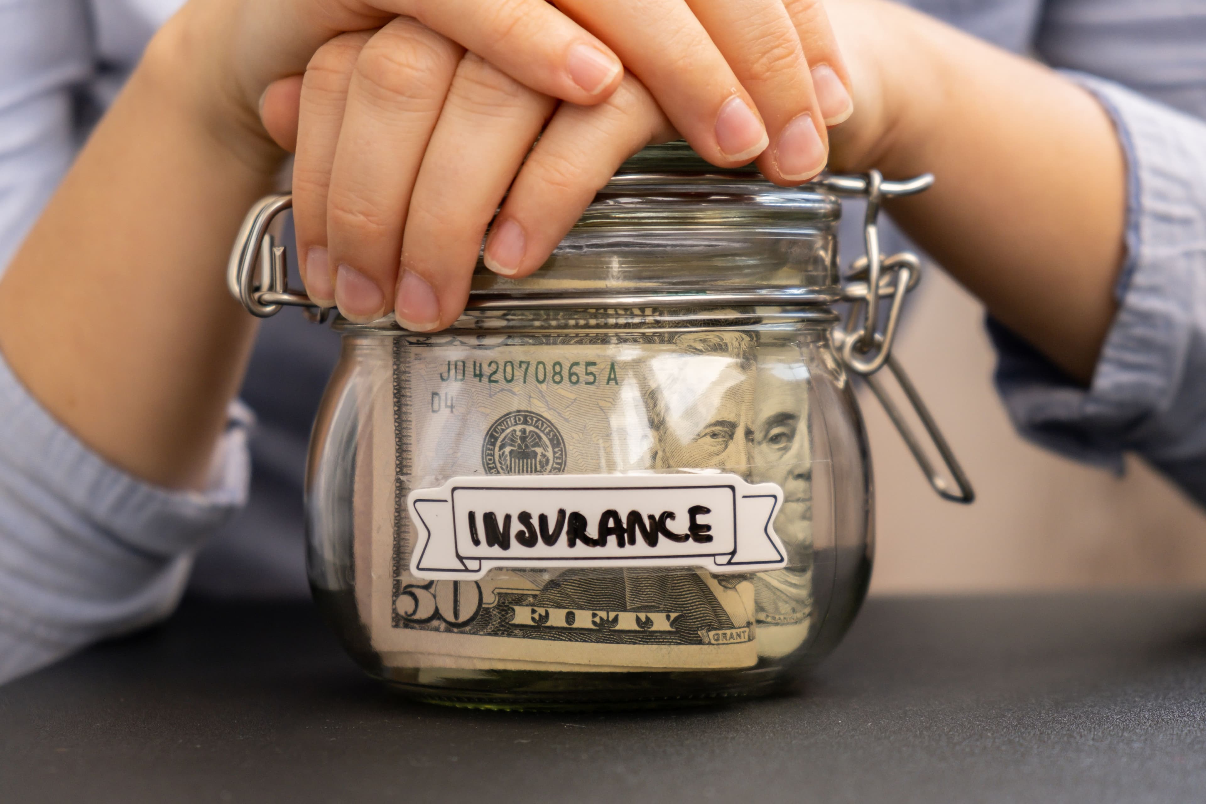 Hands holding a money jar labeled “insurance,” illustrating how self-insured companies set aside funds to pay damages.