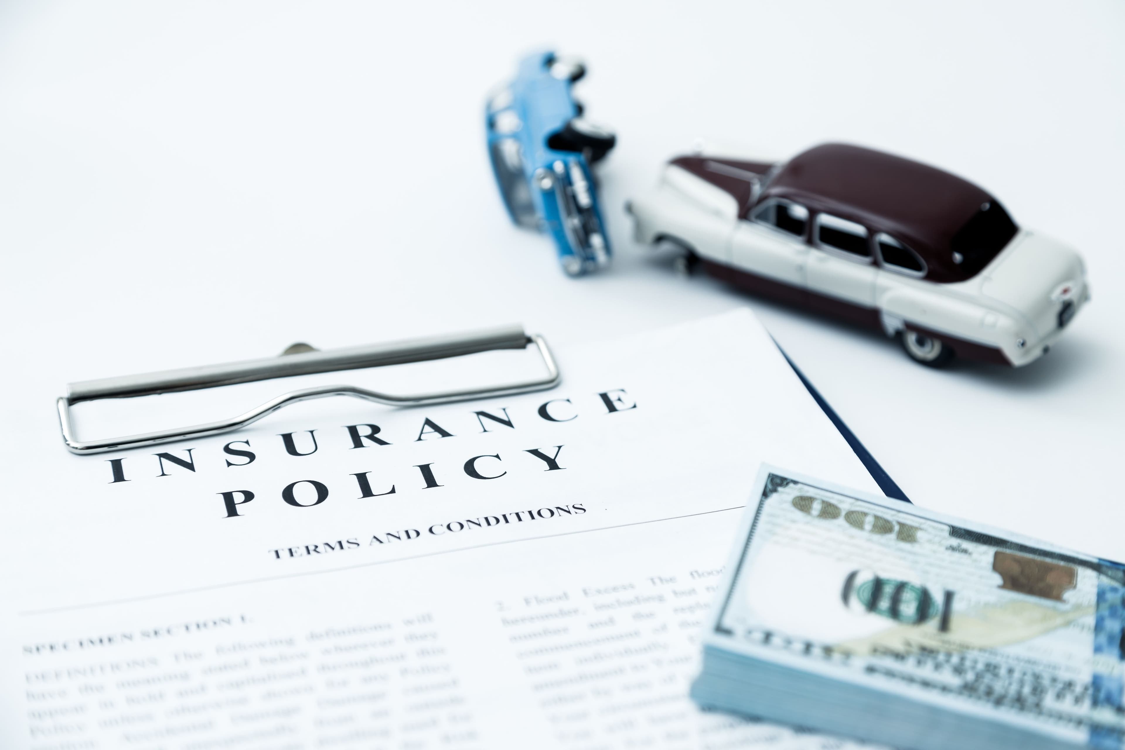 An insurance policy, toy cars mimicking a crash, and a stack of cash, indicating the impact of tort insurance on compensation.