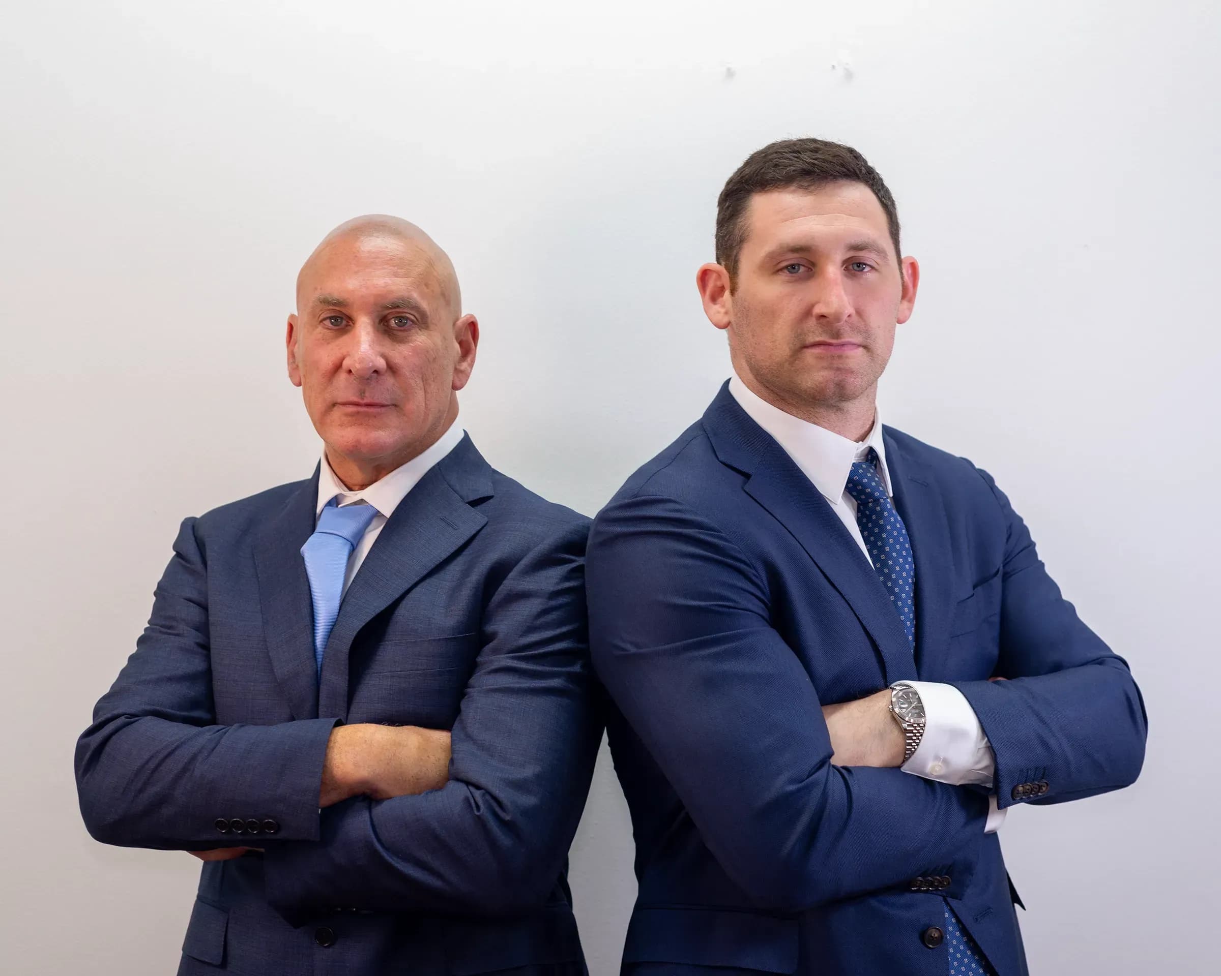 Personal injury lawyers Scott and Alex Senft standing back-to-back with arms crossed.